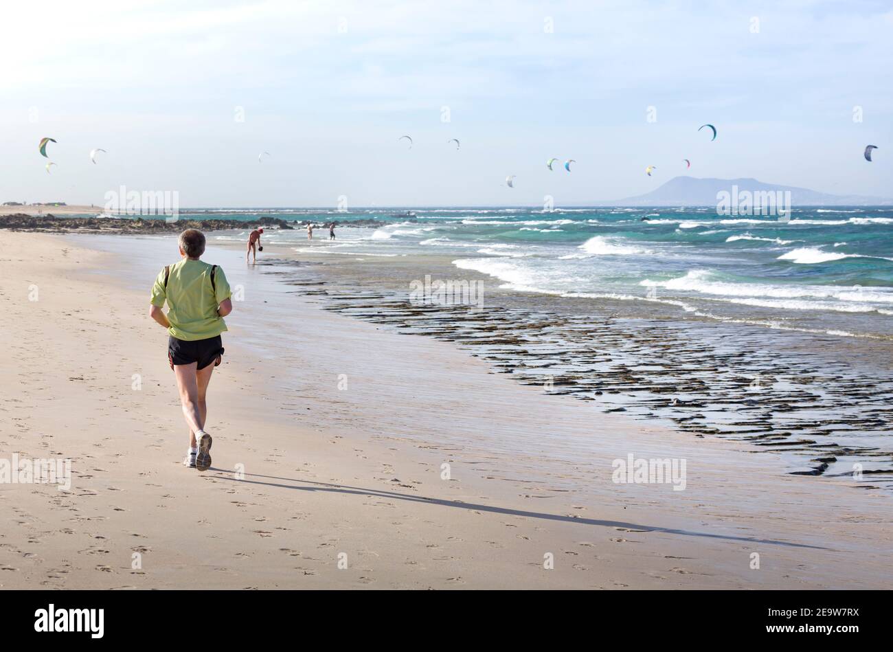 FUERTEVENTURA, SPANIEN - 10. Mai 2013. Reifer Mann beim Joggen am Strand mit Kitesurfern im Hintergrund. Corralejo, Fuerteventura, Kanarische Inseln Stockfoto