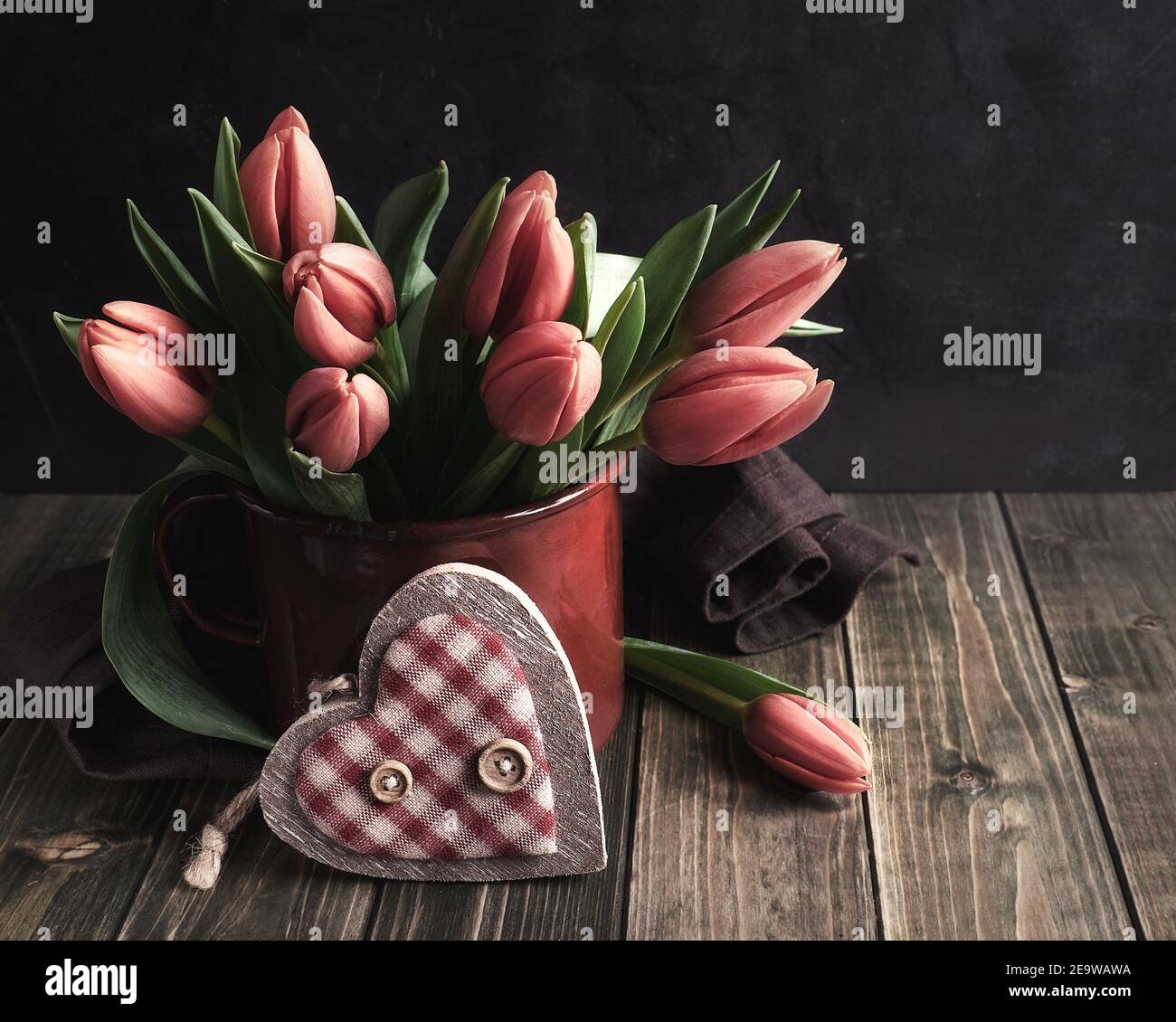 Retro Metalldose mit rot-orangen Tulpen auf dunklem rustikalem Holz. Dekoratives Holz Textil Herz. Zero Waste natürliche Osterarrangement in rot, grün, braun. Stockfoto