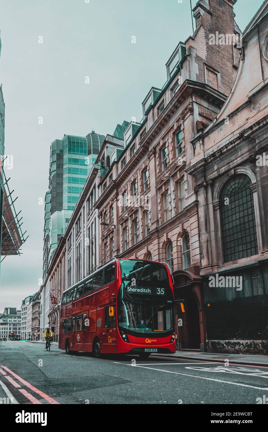 London UK Januar 2021 Vertikale Aufnahme eines modernen roten Doppeldeckerbusses, der in abgesperrten, riesigen Wolkenkratzern auf den leeren Straßen Londons fährt Stockfoto