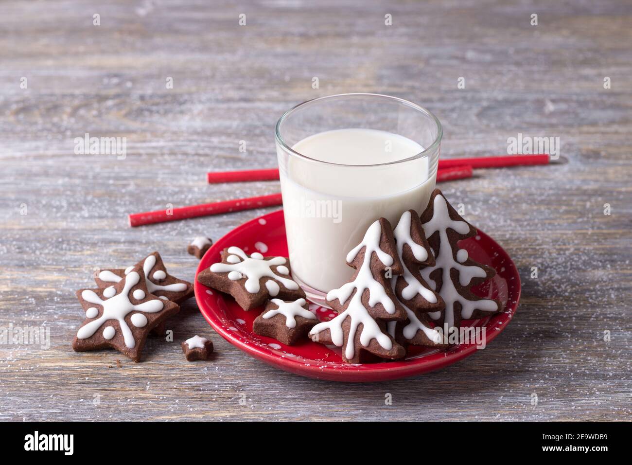 Hausgemachte Weihnachts-Schokoladenkekse, dekoriert mit Glasur, mit einem Glas Milch auf einem Holztisch. Selektiver Fokus. Horizontal Stockfoto