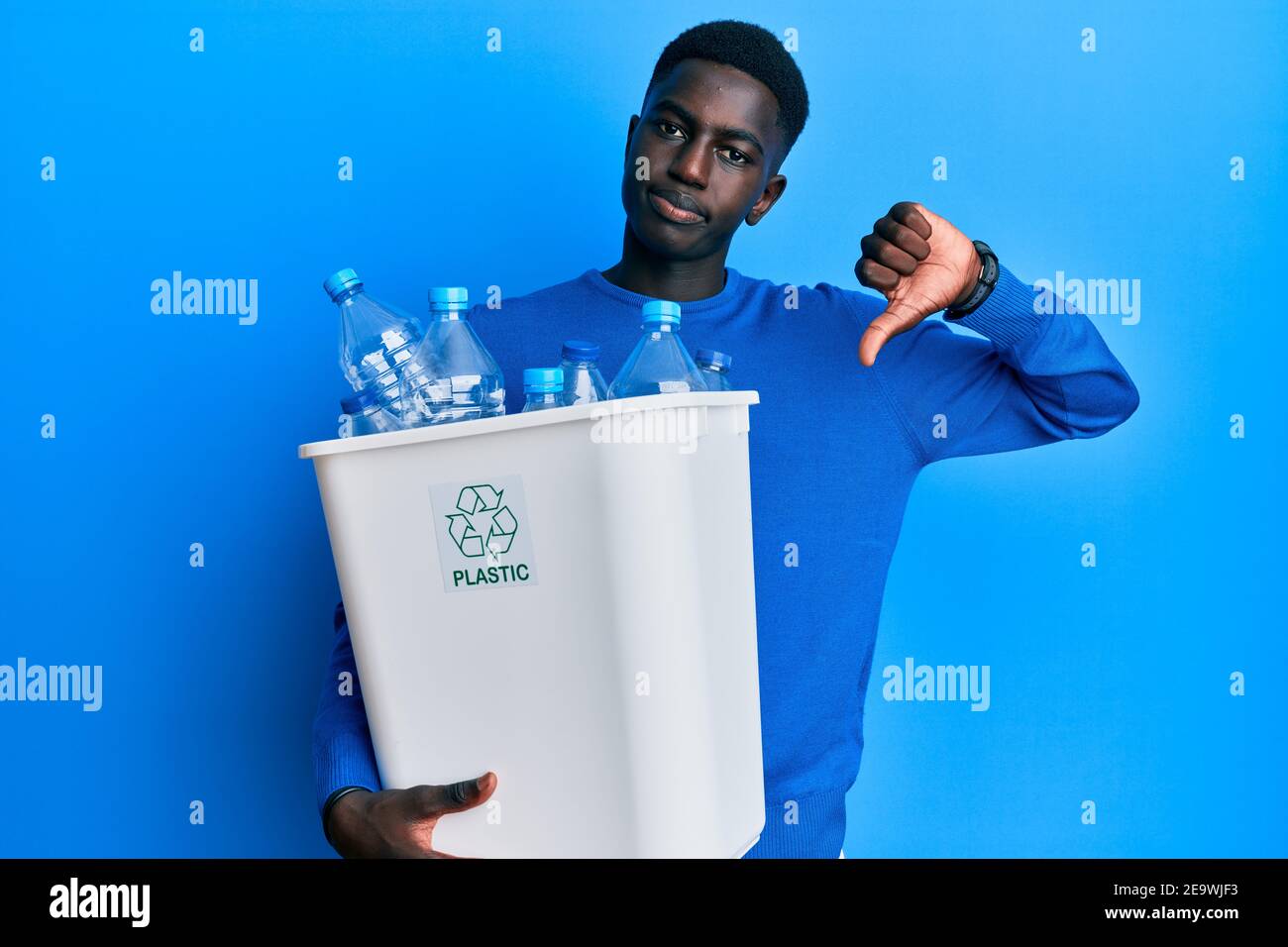 Junger afroamerikanischer Mann hält Recycling-Papierkorb mit Plastikflaschen mit wütendem Gesicht, negative Zeichen zeigt Abneigung mit Daumen nach unten, rejecti Stockfoto