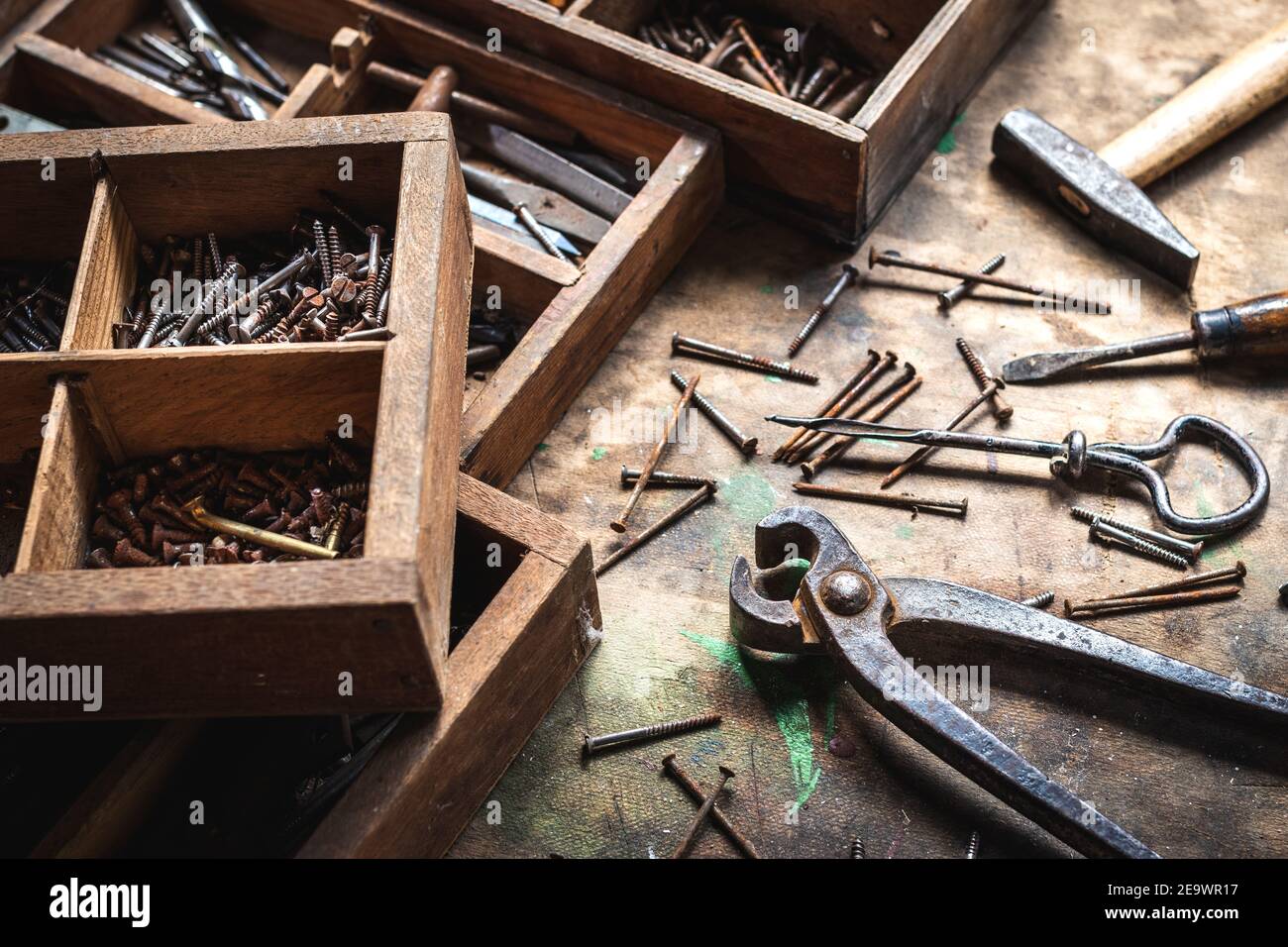 Vintage-Arbeitswerkzeug und Werkzeugkasten auf Holztisch. Chaotische Industrieanlagen in der Schreinerei Werkstatt. Zange, Schraubendreher, Hammer, Handbohrer und viele Nagel Stockfoto