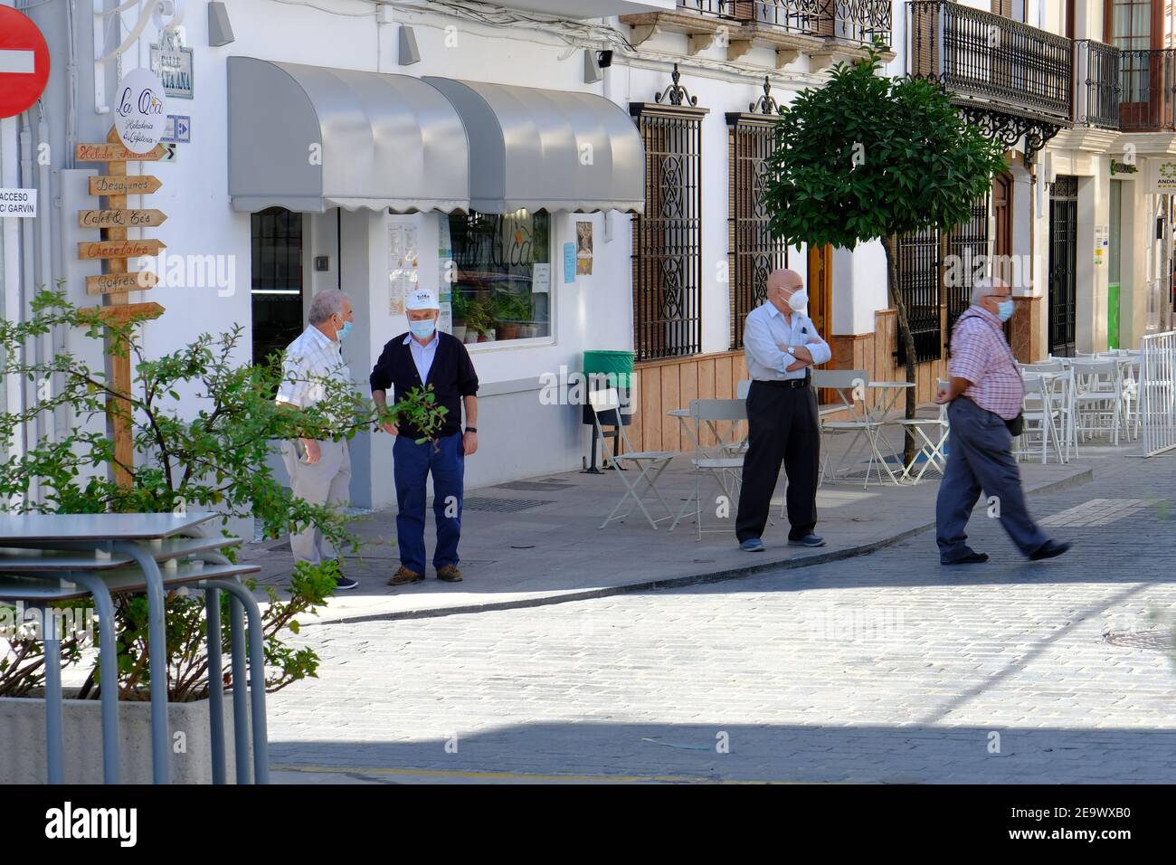 Ältere männliche Bewohner auf dem Dorfplatz, mit Masken und Distanzierung während der Covid-Pandemie im Sommer 2020. Carcabuey, Andalusien, Spanien Stockfoto