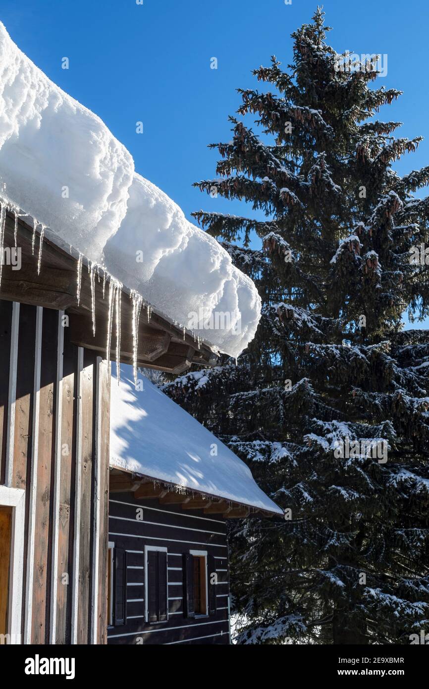 Schneebedeckte Berghütte mit Eiszapfen am sonnigen Wintertag Stockfoto