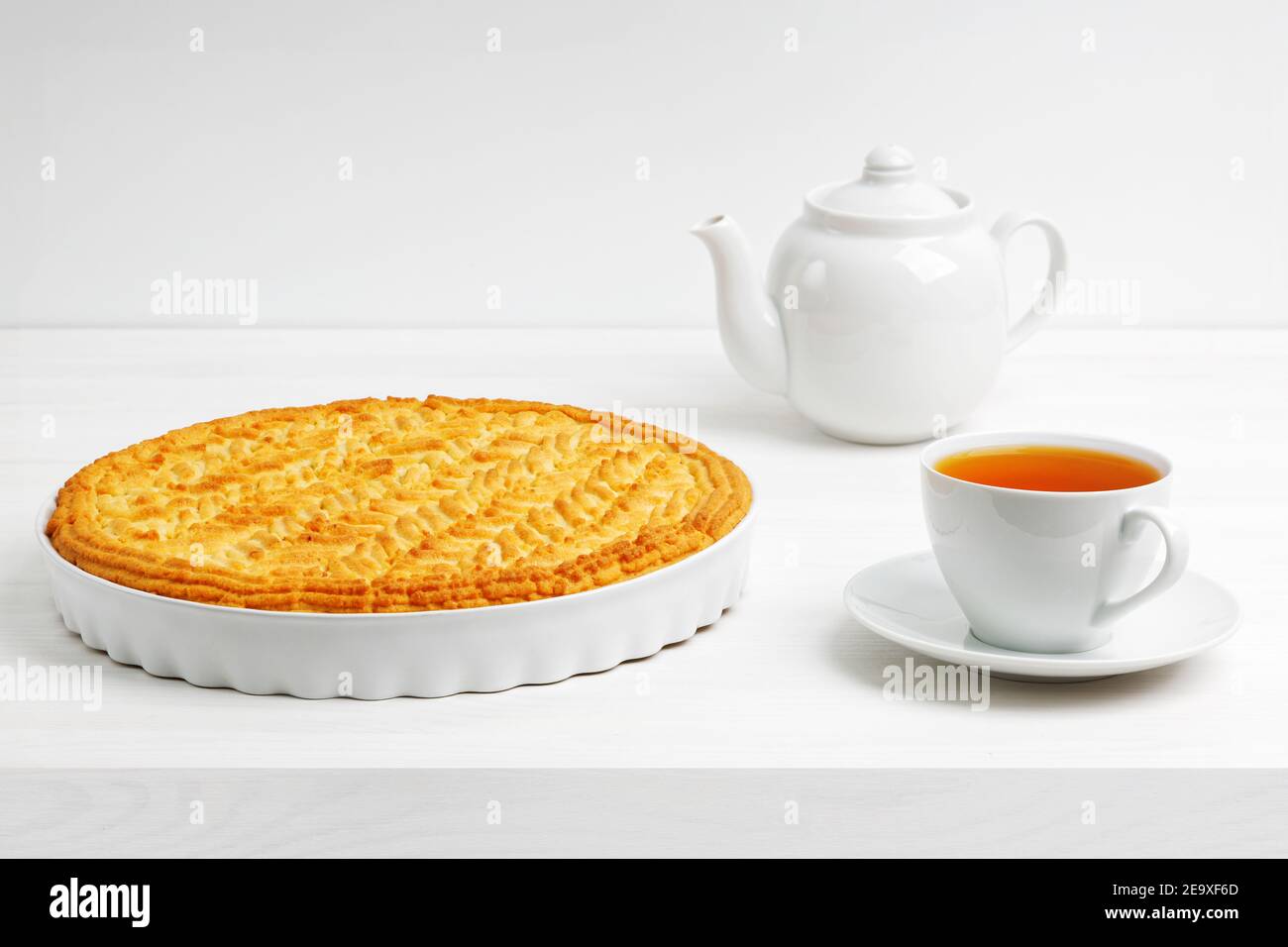 Hausgemachter Zitronenkuchen mit Stachelbeere und Tasse Tee auf weißem Holztisch. Copyspace. Stockfoto