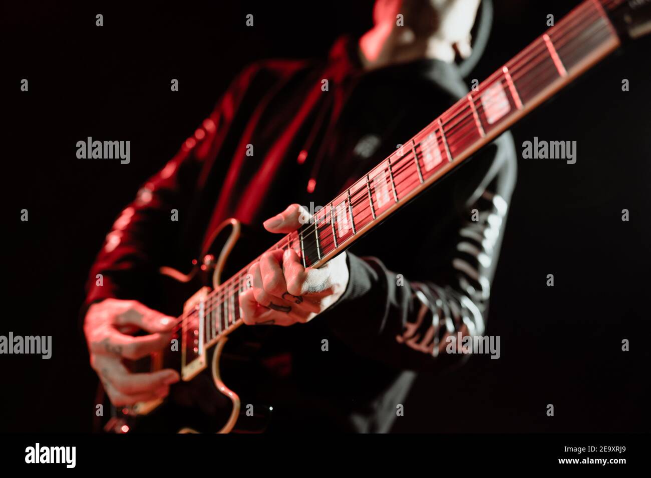 Niedriger Winkel der Rock-Gitarrist spielt E-Gitarre während der Durchführung Im dunklen Studio mit rotem Licht Stockfoto