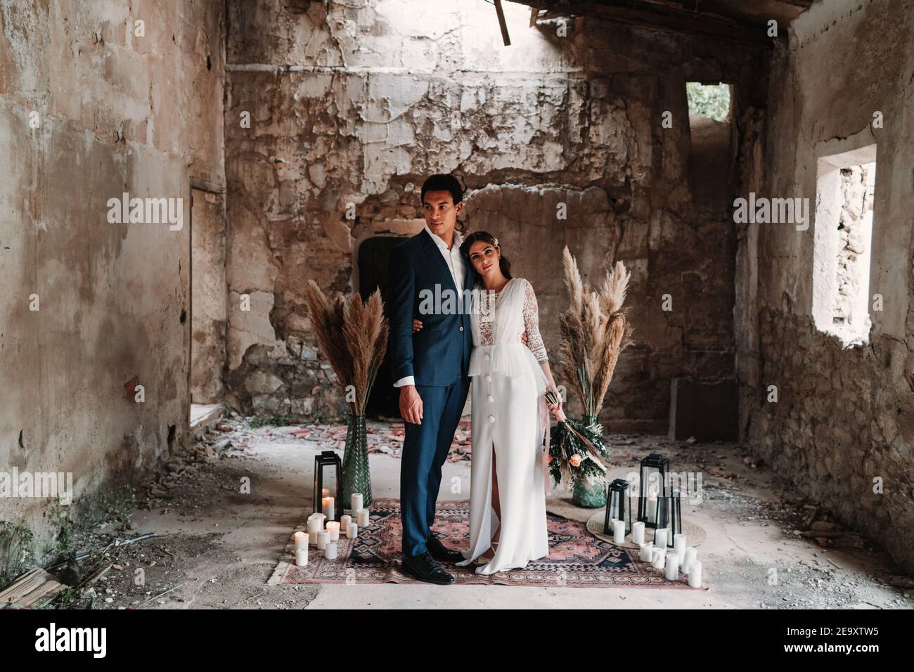 Seitenansicht Ganzkörper liebevolle junge ethnische Neuvermählte Paar tragen Chic Hochzeitskleidung umarmt und küsst sanft in obsolete Rest Gebäude Stockfoto