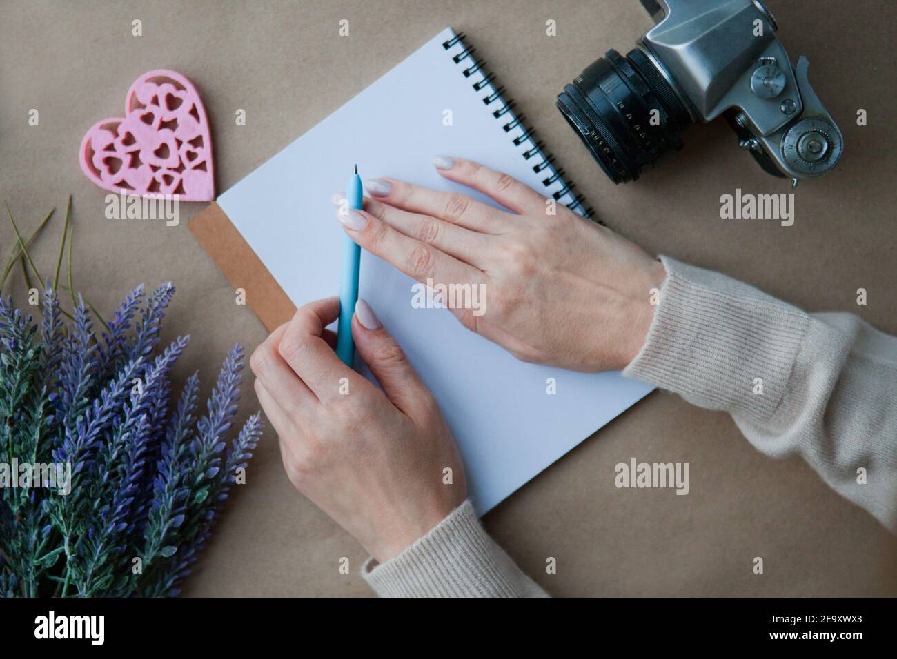 Holzherz LIEBE und Frau Hände hinter Notebook auf dem Tisch und Retro-Kamera. Konzept für das Schreiben von Briefen. Symbol für Herzform. Valentinstag - romantisch Stockfoto