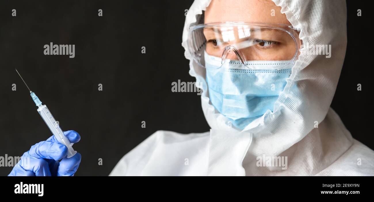 Der Arzt in persönlicher Schutzausrüstung (PSA) hält eine Spritze für die COVID-19-Impfstoffinjektion. Portrait der Krankenschwester trägt Gesichtsmaske und Brille. Konzept o Stockfoto