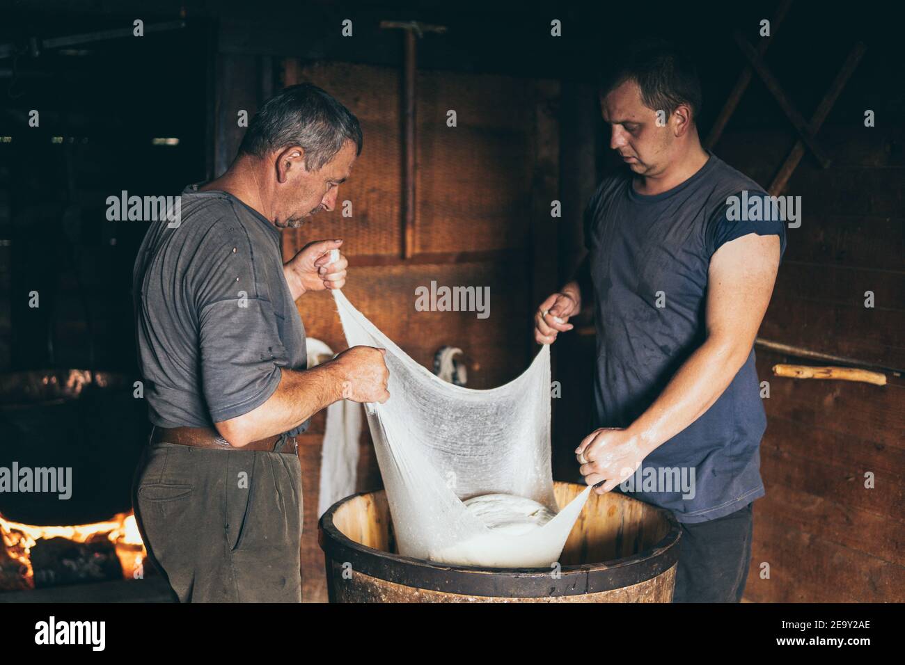 Karpaten, Ukraine - August 2020: Zwei Männer, die Bauernkäse machen. Die Molke durch die Käseschachtel abtropfen lassen. Stockfoto