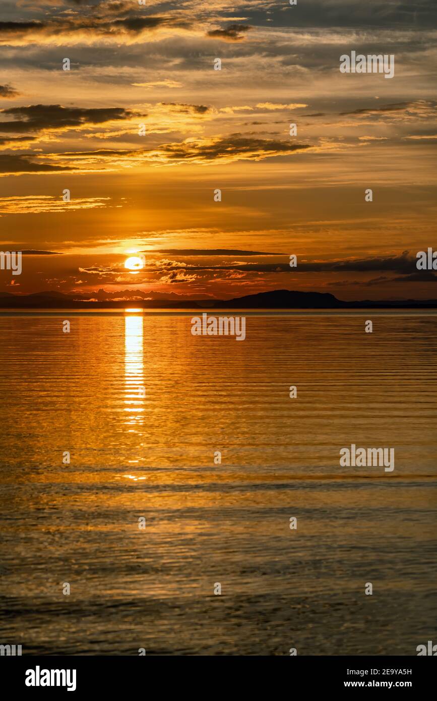 Vertikales Foto des Sonnenuntergangs über Umea River Mountains, Sommerhimmel mit Wolken durch orange rote Sonne hervorgehoben. Sonnenlicht Pfad auf Wasser Storuman, Lappland, SW Stockfoto