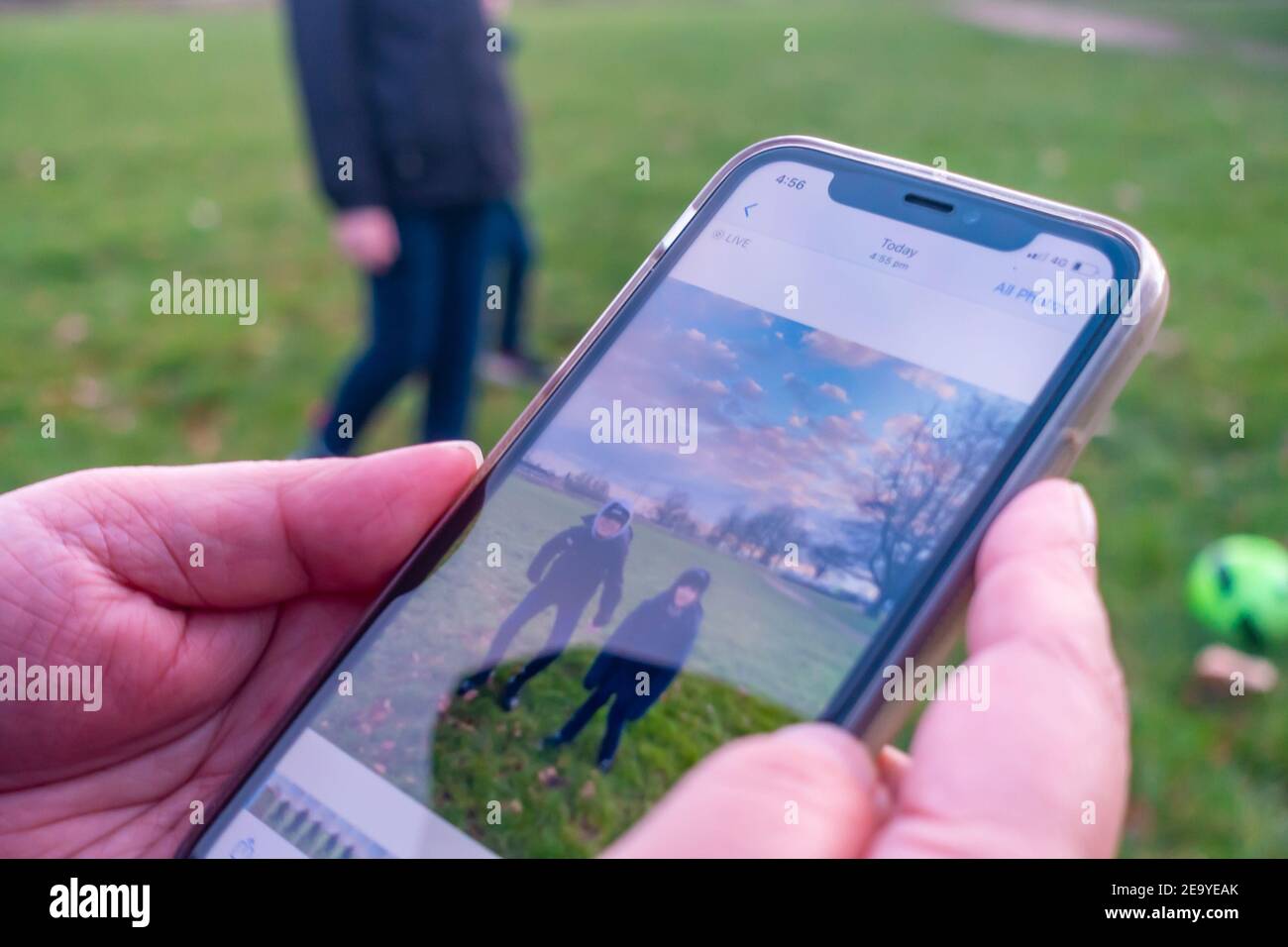 Eine Frau, die nur Hände sichtbar hat, überprüft ein Foto ihrer Kinder, das auf ihrem iPhone im Park aufgenommen wurde. Stockfoto