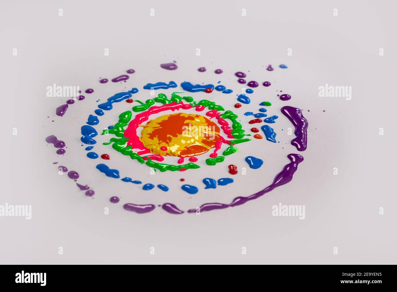 Farben fallen auf einen sich drehenden weißen Hintergrund. Die Farbe der Tropfen ist ein kreisförmiger Halo Stockfoto