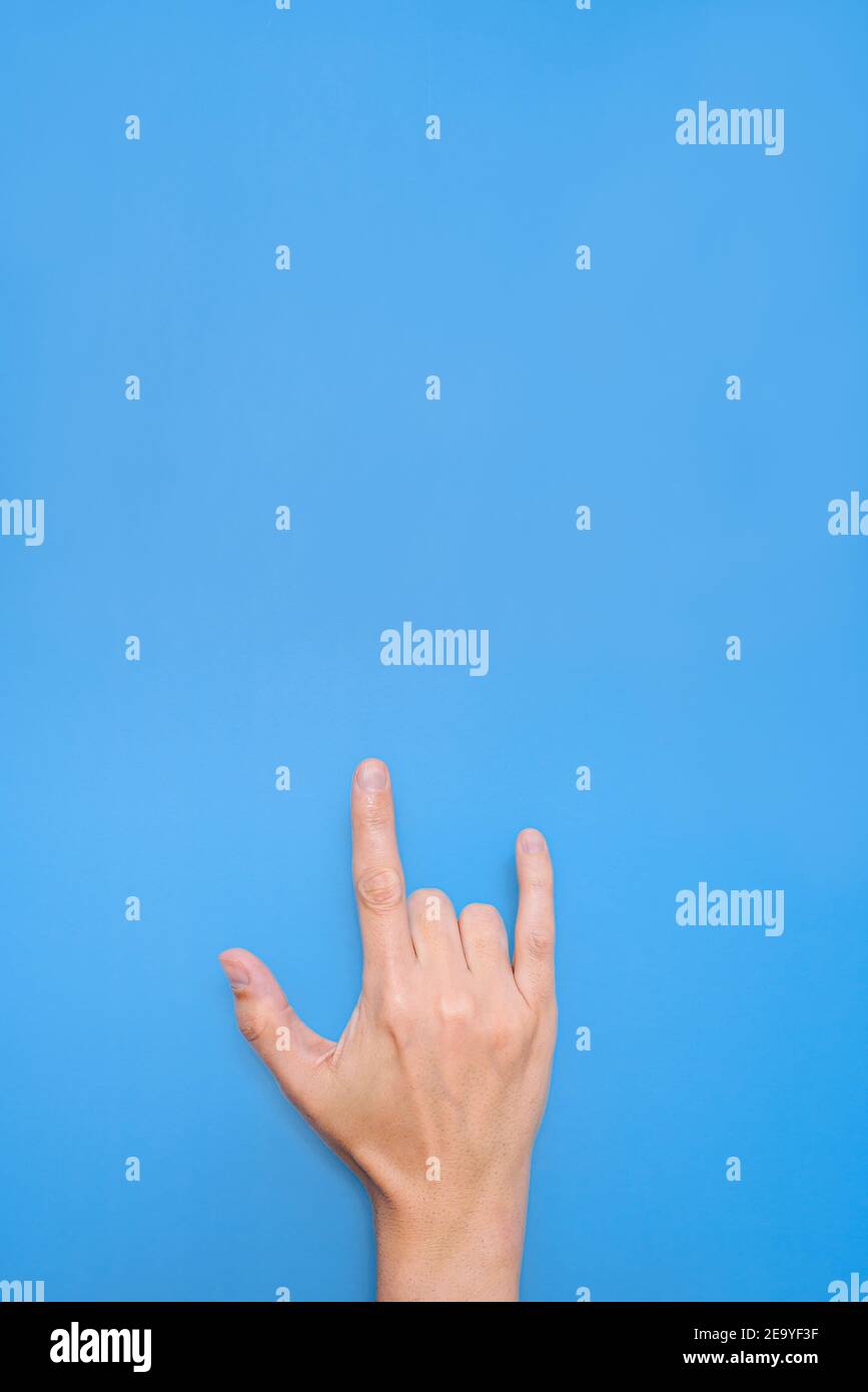 Vertikale Übernahme der Hand eines nicht erkennbaren kaukasischen Mannes Tun Symbol der Liebe mit einem blauen Hintergrund Stockfoto