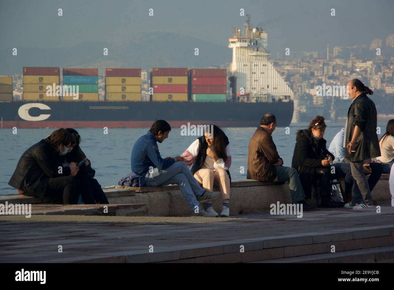 Menschen versammeln sich an der Strandpromenade von Alsancak, Izmir, während das Containerschiff in der Bucht vorbei fährt Stockfoto