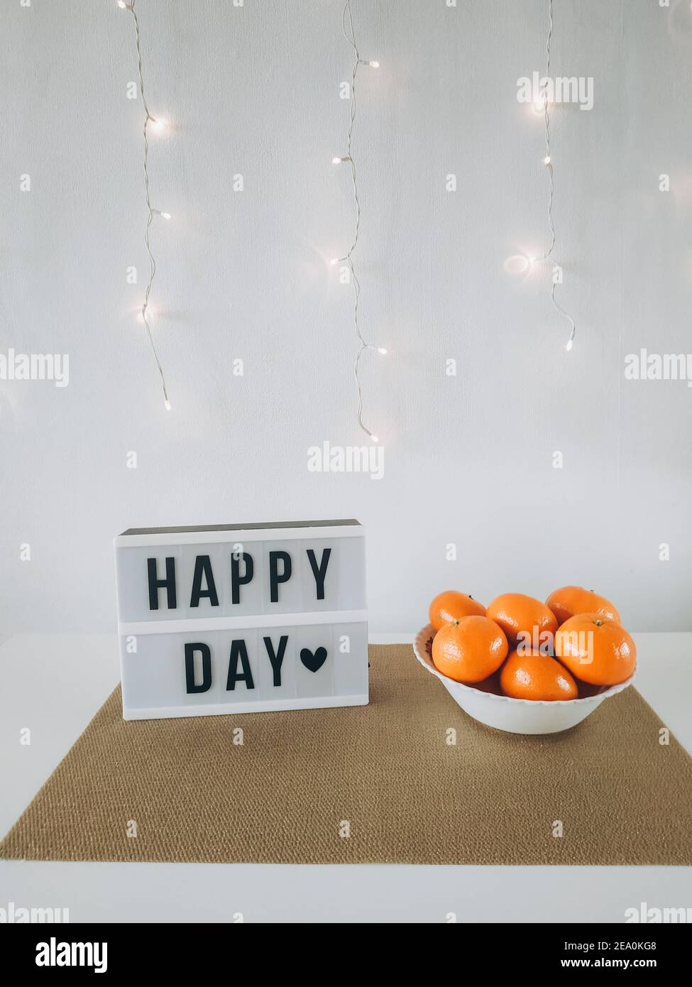 HAPPY DAY Wort auf Leuchtkasten mit Mandarinen an der Wand mit Licht Hintergrund. Gemütliches Haus compozition. Stockfoto