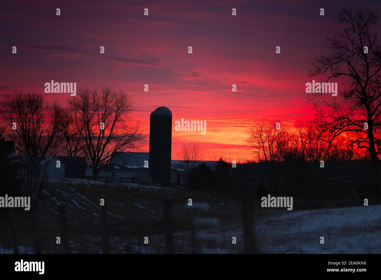 Ein Sonnenaufgangshimmel über einer kleinen Indiana Farm. Der Himmel besteht aus Rot, Gelb, Violett, Orangen und Blau. Ein Silo ist prominent gekennzeichnet. Stockfoto
