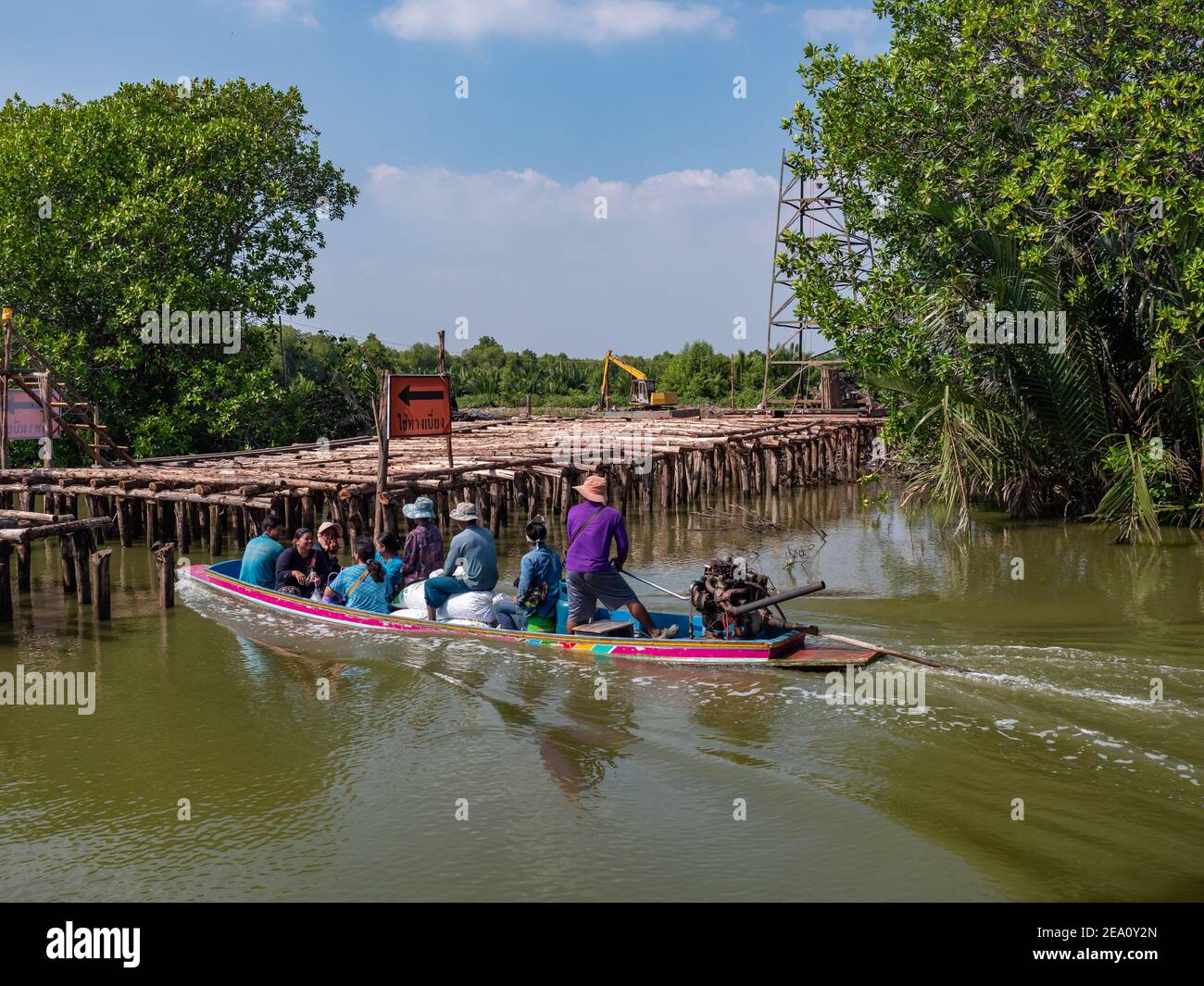 Lokale Bauern passieren eine Baustelle, auf der eine Straßenbrücke gebaut wird, auf einem traditionellen thailändischen Langschwanz-Boot auf einem Kanal zwischen Garnelen und Schellfis Stockfoto