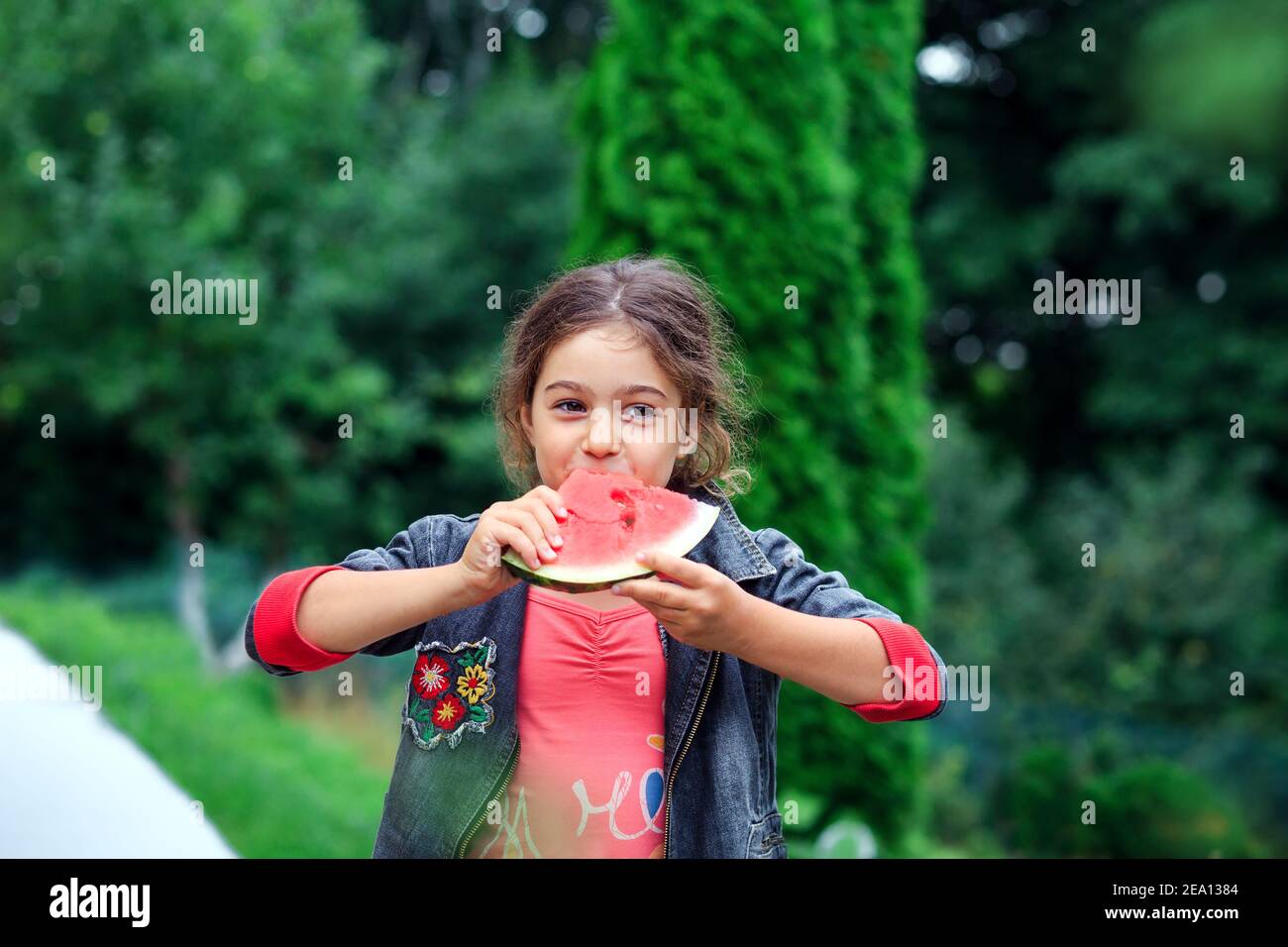 Kleines hübsches Mädchen, das im Garten eine saftige Wassermelone isst. Kinder essen Obst im Freien. Gesunde Ernährung für Kinder. Stockfoto