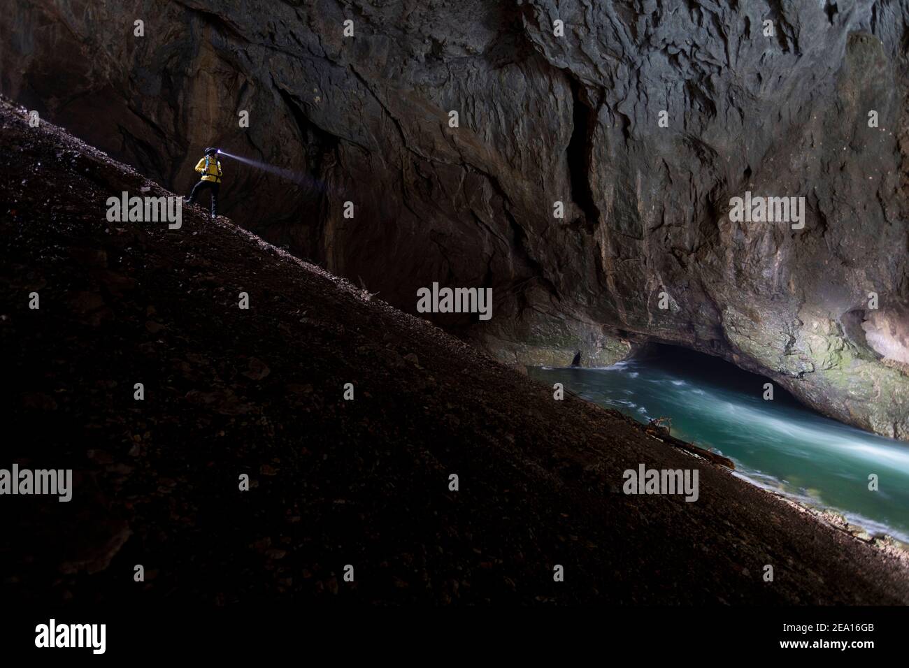 Frau mit Stirnlampe, die auf steilem Gelände am Fluss in der Tkalca-Höhle im Rakov Skocjan-Park in Slowenien steht Stockfoto