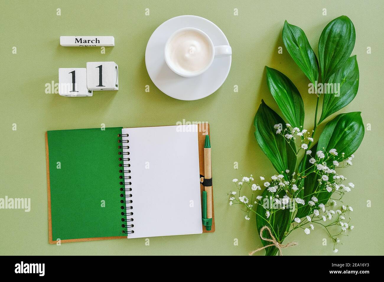 Holzwürfel Kalender März 11. Öffnen Sie leeren Notizblock, Tasse Kaffee, Blumenstrauß auf grünem Hintergrund. Konzept hallo Frühling Kreativ Draufsicht Flat la Stockfoto