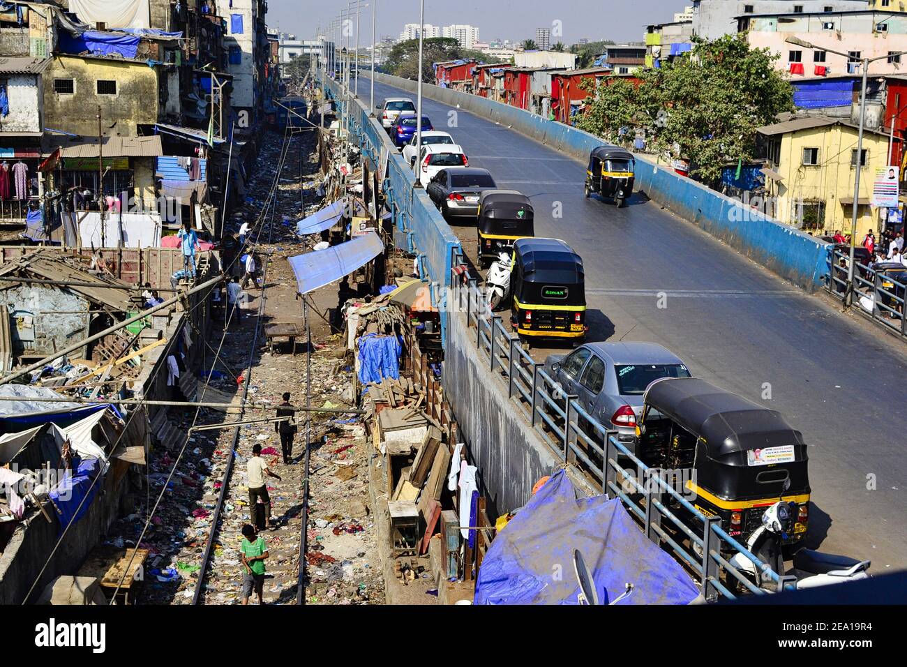 Mumbai, Maharashtra, Indien - Dezember 2016: Geparkte Tuk Tuks und Autos auf der Straßenbrücke entlang der Eisenbahnstraße in der Nähe von schmutzigen Slums und Wohnhäusern Stockfoto