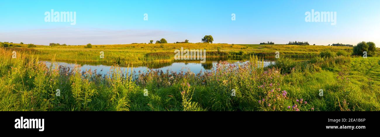 Sommer Panorama-Sonnenuntergangslandschaft mit ruhigen Fluss und grünen Hügeln während sonnigen Abend. Stockfoto