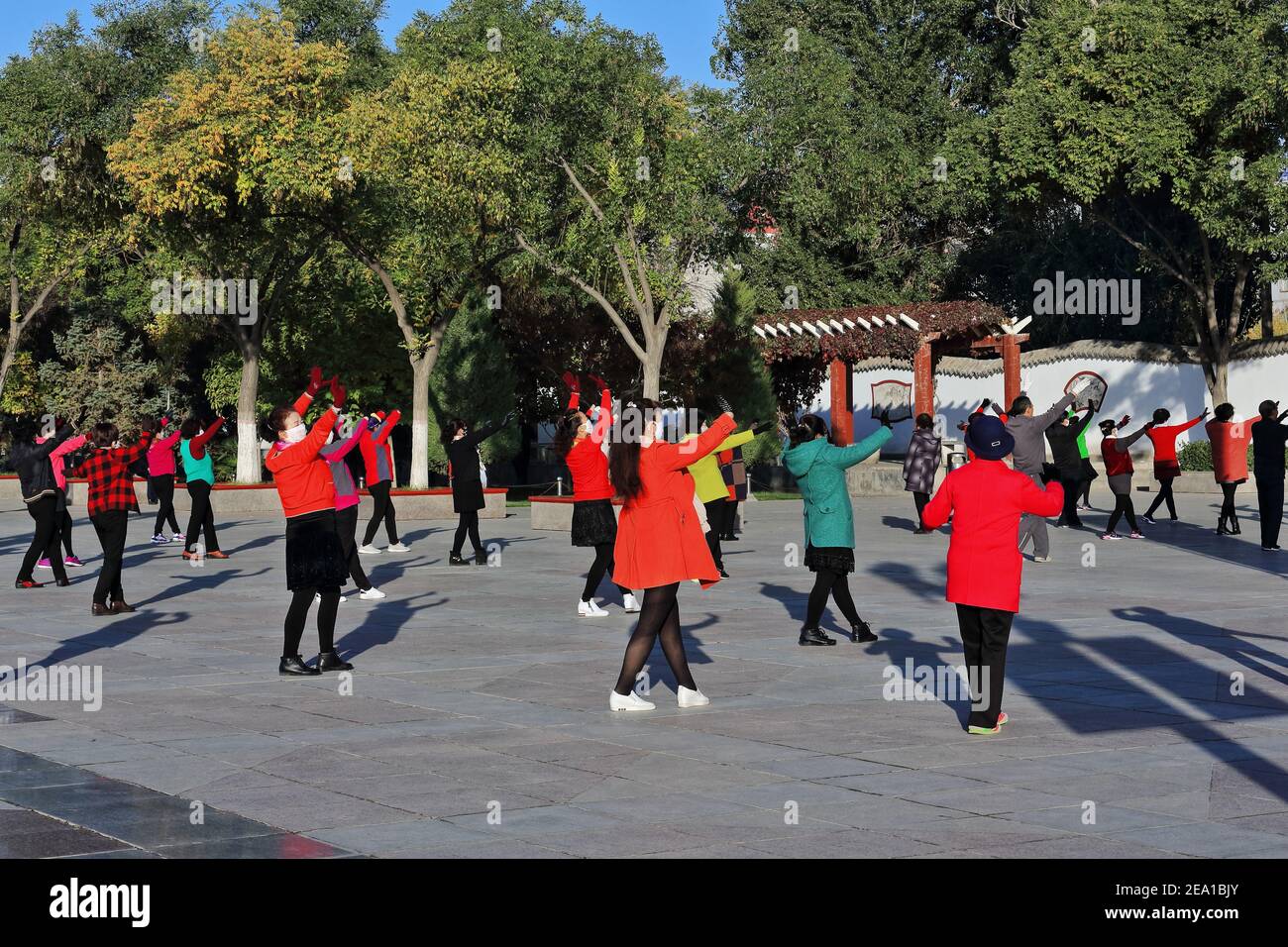 Maskierte Gruppentänzer in der frühen Morgensonne führen Gymnastik durch Choreografien zum Klang tragbarer Musik wie zu Halten Sie ihre körperliche Fitness Stockfoto