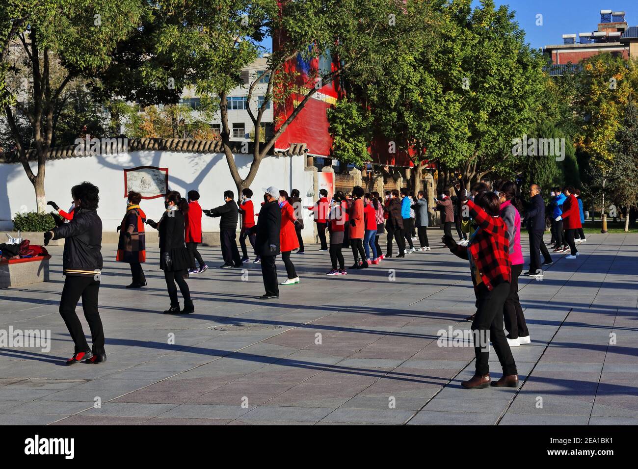 Maskierte Gruppentänzer in der frühen Morgensonne führen Gymnastik durch Choreografien zum Klang tragbarer Musik wie zu Halten Sie ihre körperliche Fitness Stockfoto