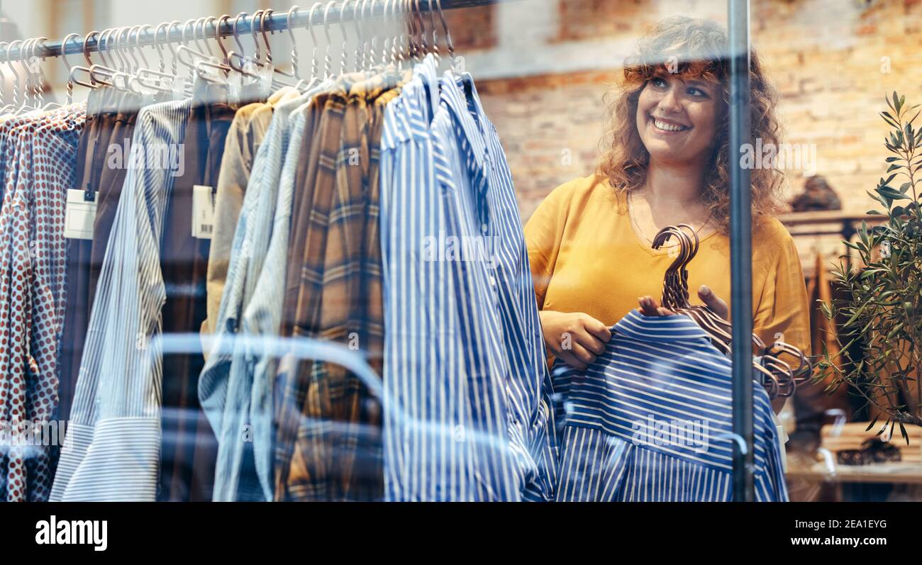 Frau, die in einem Bekleidungsgeschäft arbeitet. Frau hängend neue Kleidung auf Rack im Laden. Stockfoto