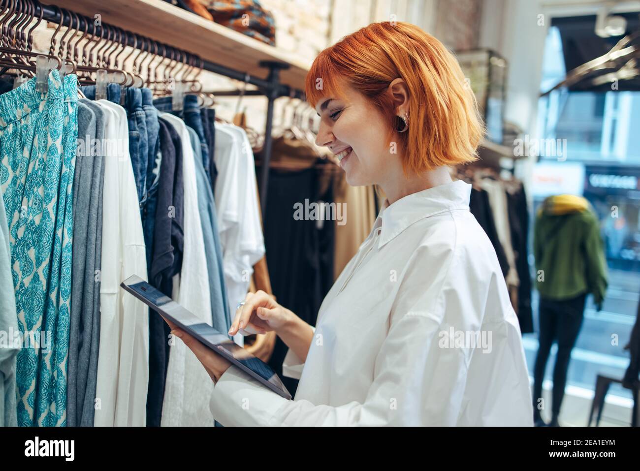 Frau lächelt, während sie ihr digitales Tablet in ihrem Geschäft benutzt. Unternehmerin in ihrer Boutique mit digitalem Tablet. Stockfoto