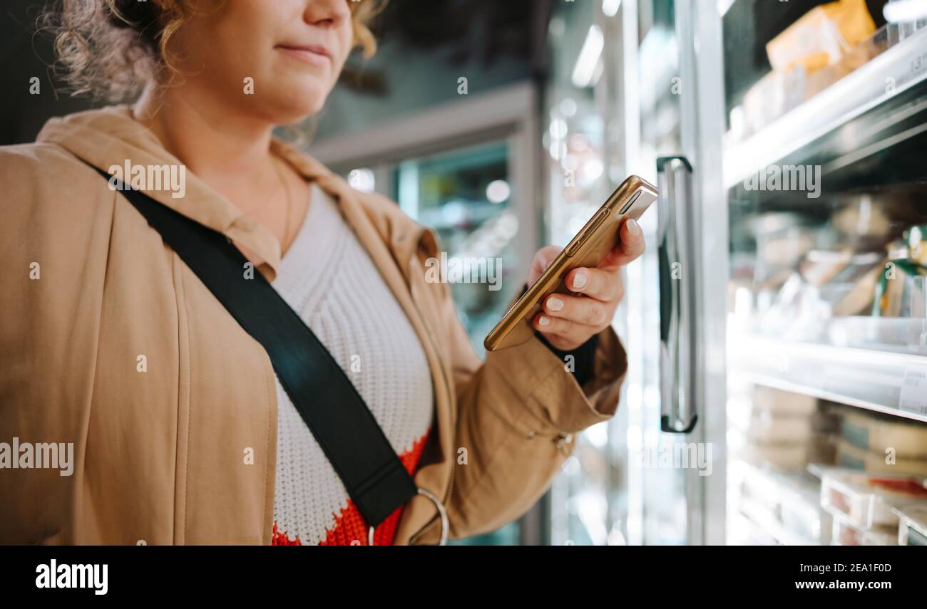 Shopper, der die Einkaufsliste auf ihrem Handy ansieht. Frau mit Handy beim Einkaufen im Supermarkt. Stockfoto