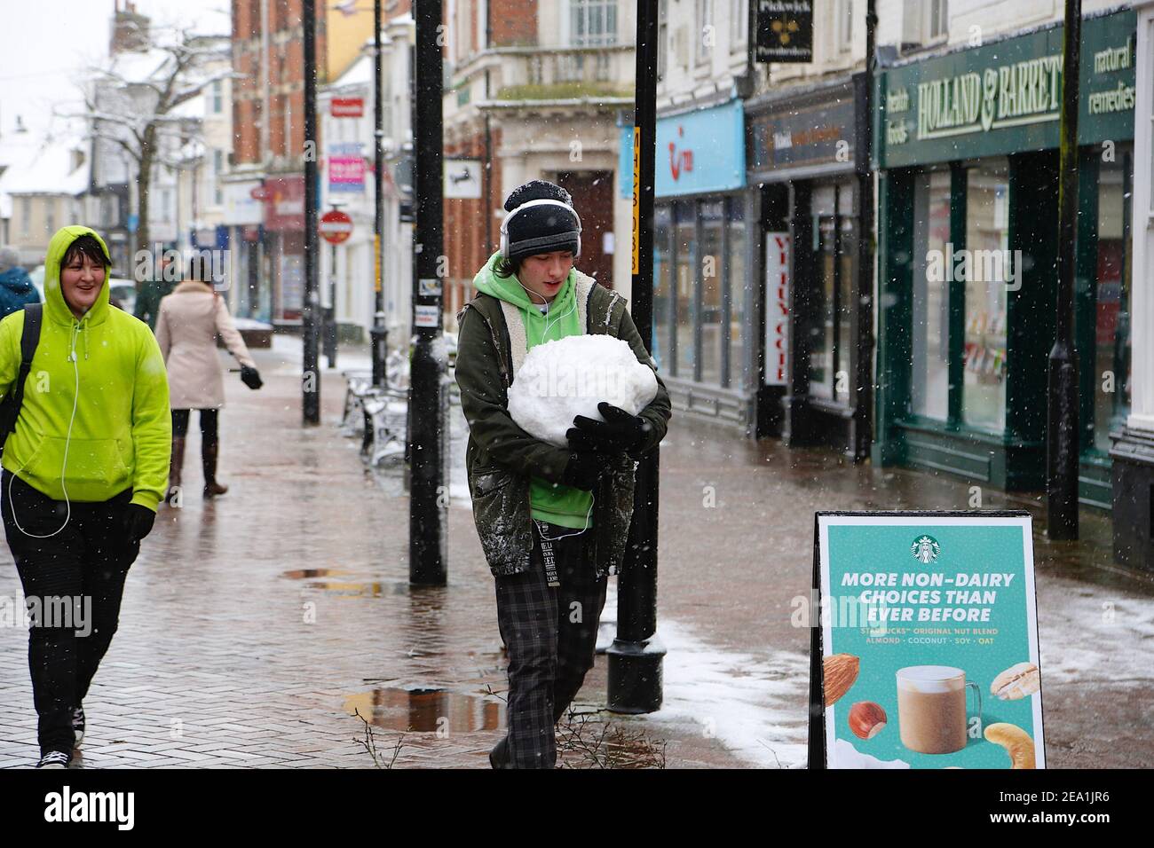 Ashford, Kent, Großbritannien. Februar 2021, 07. UK Wetter: Sturm Darcy trifft die Stadt Ashford in Kent. Ein junger Mann trägt einen Schneeball entlang der Hauptstraße. Foto-Kredit: Paul Lawrenson/Alamy Live Nachrichten Stockfoto