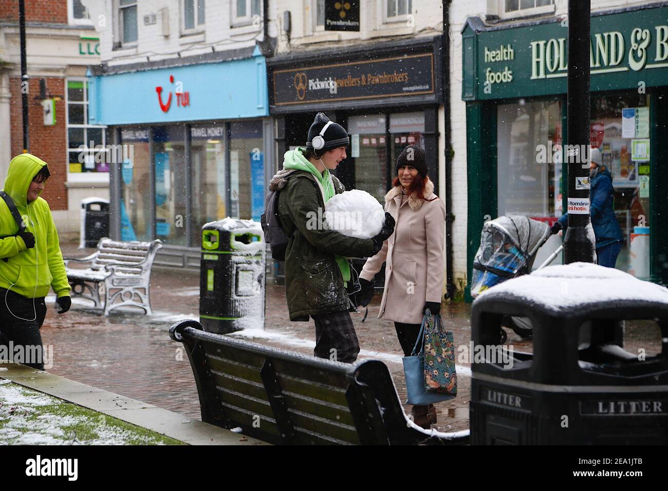 Ashford, Kent, Großbritannien. Februar 2021, 07. UK Wetter: Sturm Darcy trifft die Stadt Ashford in Kent. Ein junger Mann trägt einen Schneeball entlang der Hauptstraße. Ein Passant fragt, was er gerade tut. Foto-Kredit: Paul Lawrenson/Alamy Live Nachrichten Stockfoto