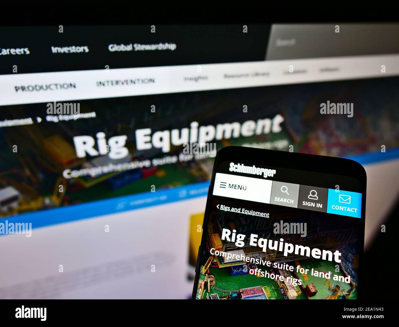 Mobiltelefon mit Business-Webseite und Logo des Ölfelddienstleisters Schlumberger auf dem Bildschirm vor dem Monitor. Fokus auf Handy-Display. Stockfoto