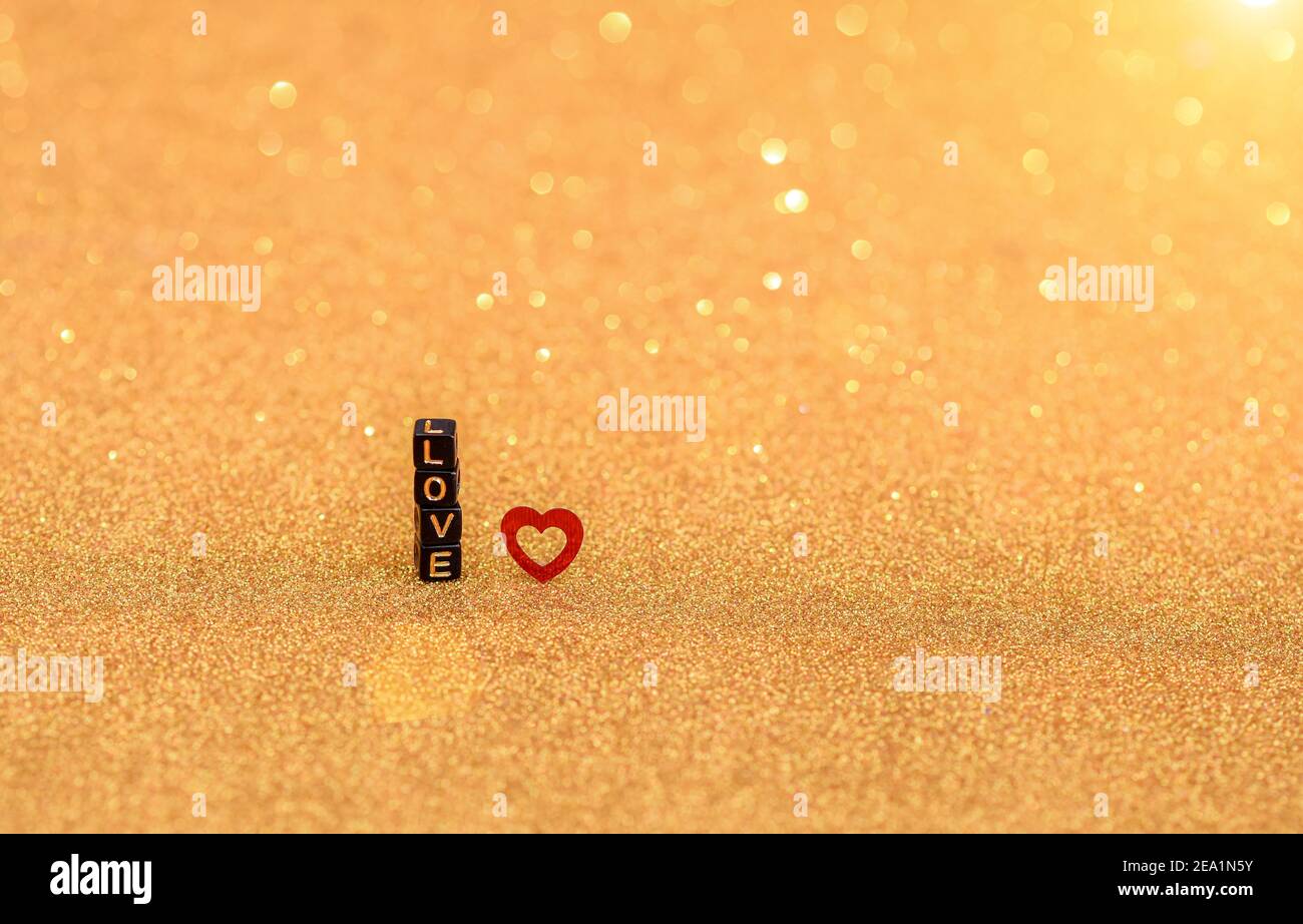 Die Inschrift Love aus Holzbuchstaben und Herzchen auf goldenem, irisierendem Hintergrund. Valentinstag und Liebe Konzept. Stockfoto