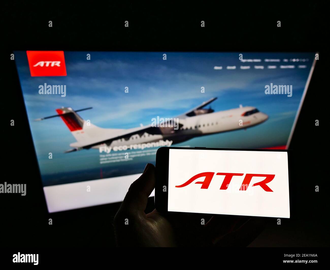 Person, die Mobiltelefon mit Logo des Flugzeugherstellers Avions de Transport Régional (ATR) auf dem Bildschirm vor der Webseite hält. Konzentrieren Sie sich auf die Telefonanzeige. Stockfoto
