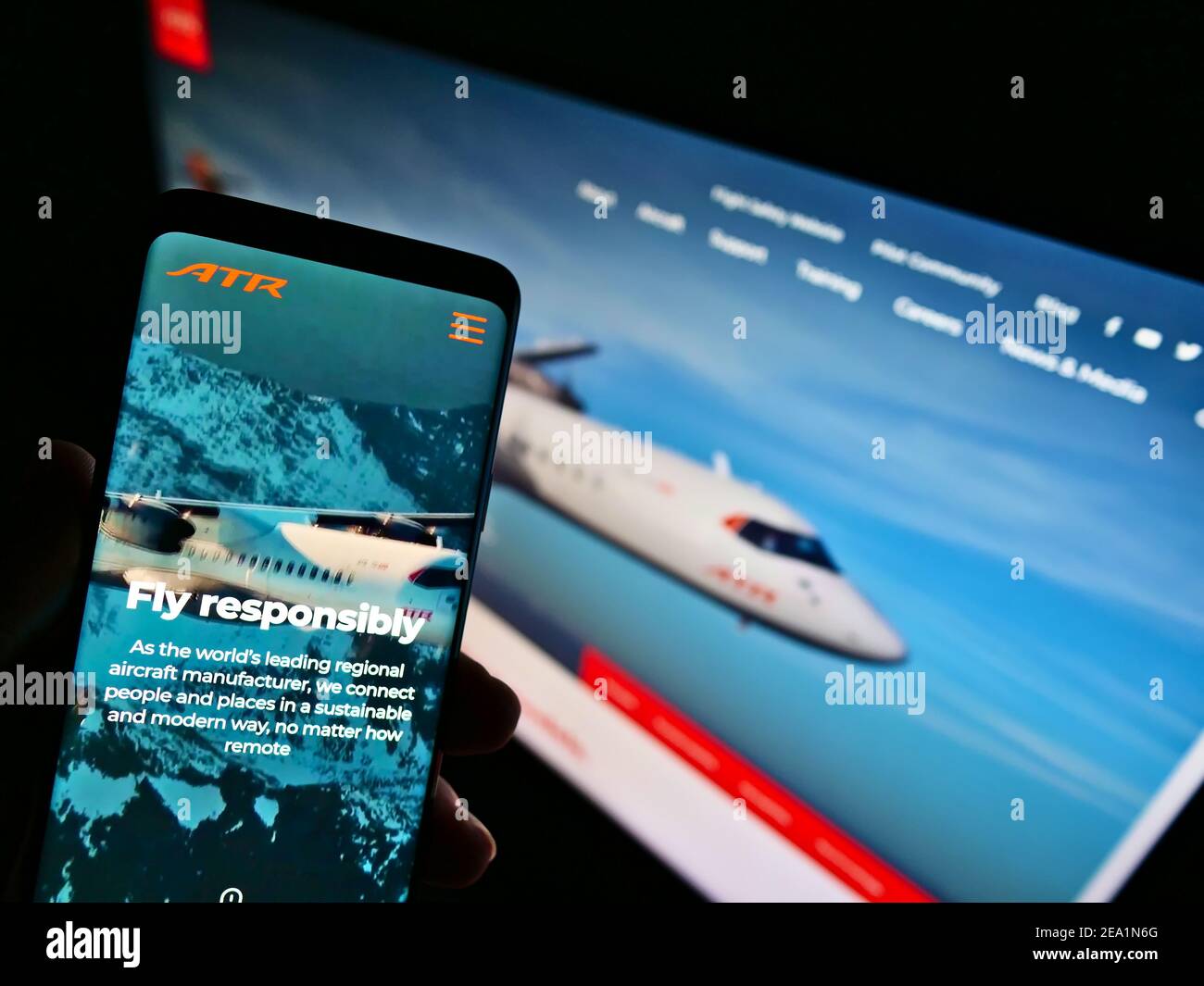 Person mit Smartphone mit Website des Flugzeugherstellers Avions de Transport Régional (ATR) auf dem Bildschirm mit Hintergrund. Konzentrieren Sie sich auf die Telefonanzeige. Stockfoto