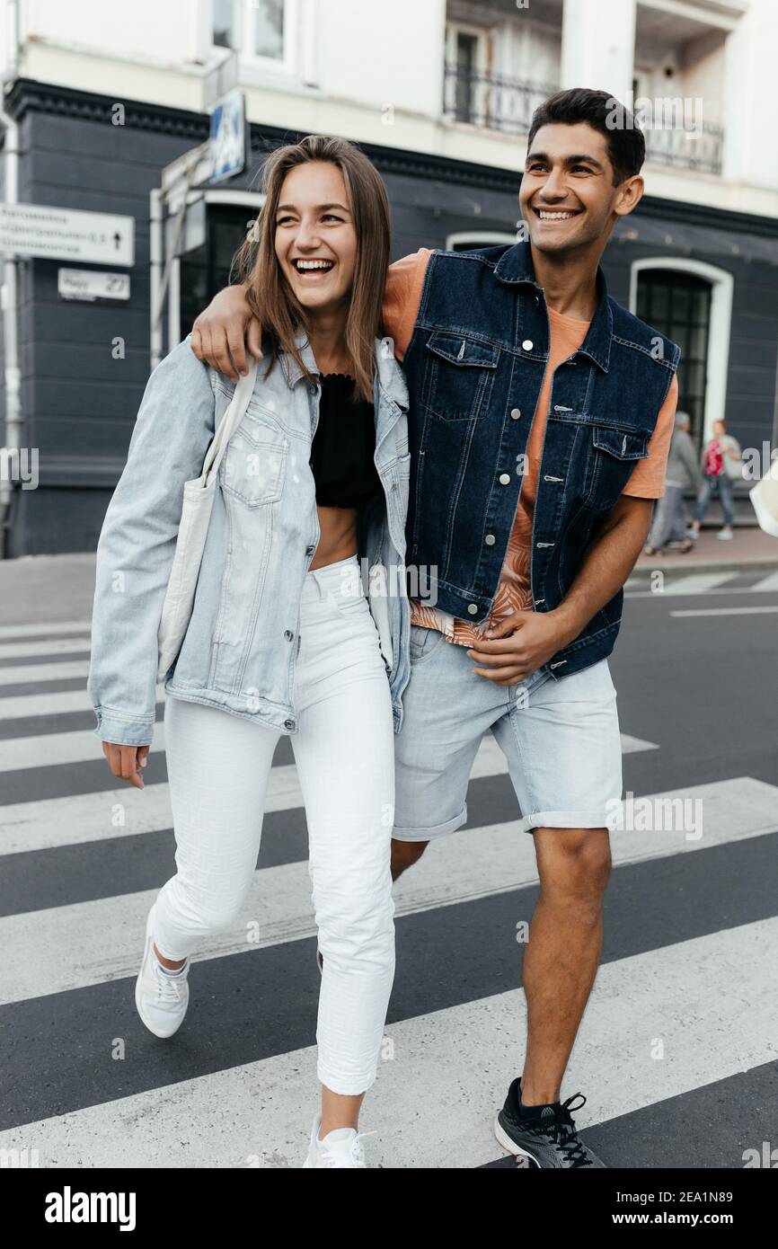 Stilvolles Paar geht auf dem Fußgängerkreuz umarmen und lächeln. Verliebte Paare in der Stadt. Urbane Liebesgeschichte Stockfoto