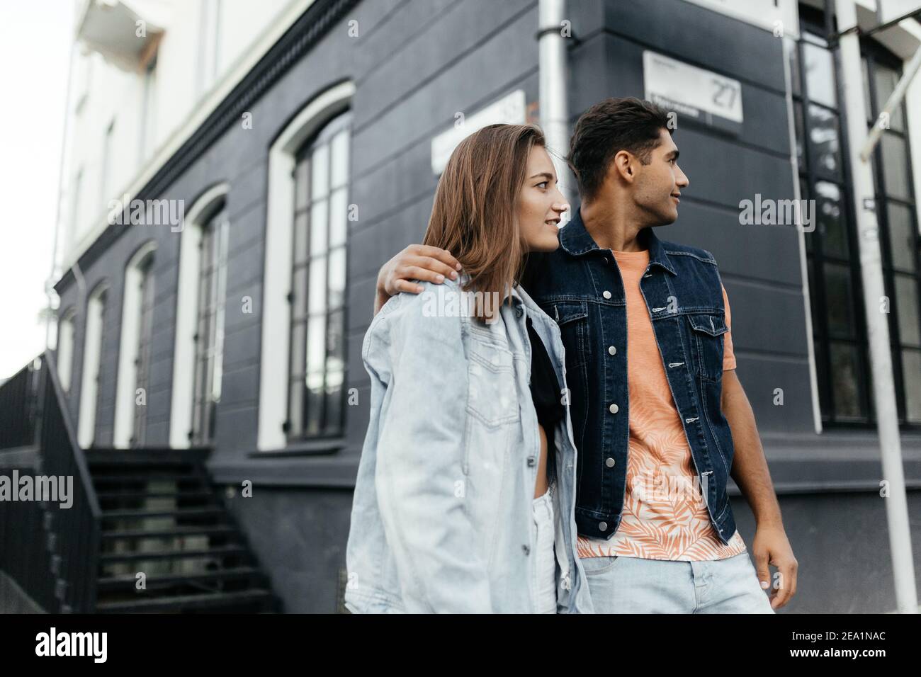 Liebhaber tragen den lässigen Stil, der zur Seite schaut, während sie vor einem verschwommenen Gebäude stehen. Verliebte Paare in der Stadt. Urbane Liebesgeschichte Stockfoto
