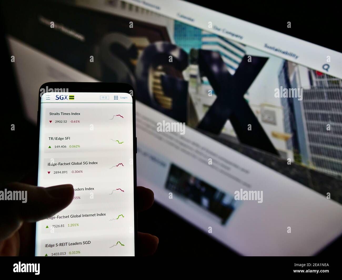 Person hält Handy mit Indizes der Börse Singapur Exchange (SGX) auf dem Bildschirm vor der Webseite. Fokus auf der Mitte des Telefondisplays. Stockfoto