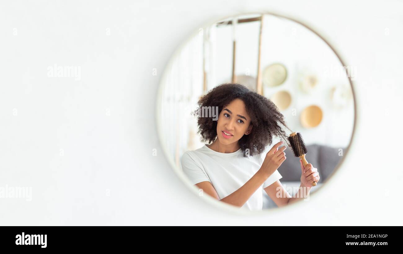 Verärgerte tausendjährige afroamerikanische Frau fühlen Schmerz tun Frisur, Blick in Reflexion von runden Spiegel Stockfoto