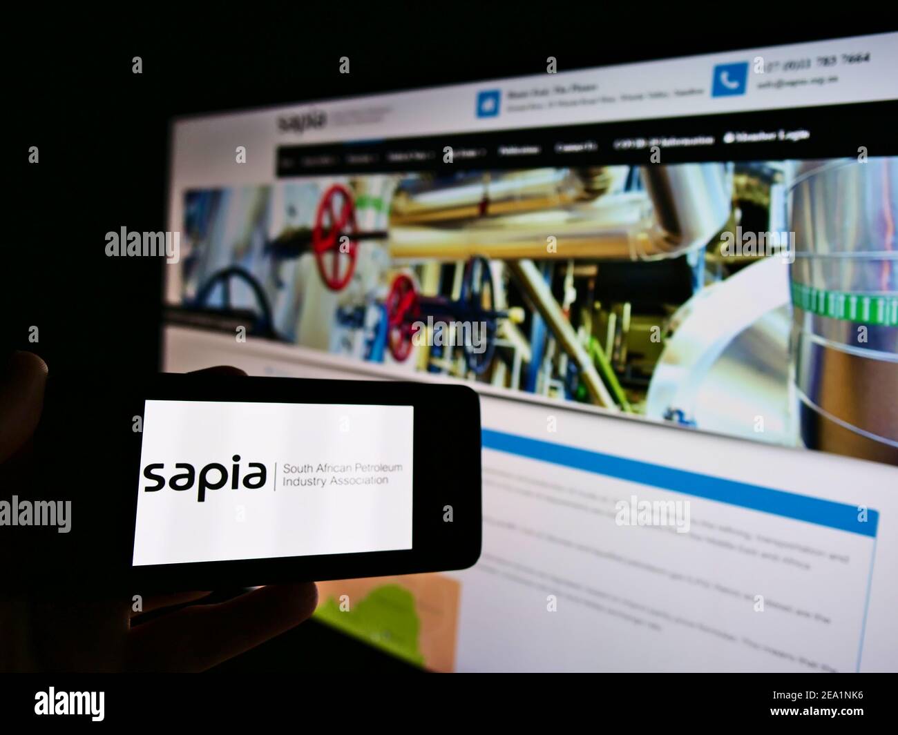 Person mit Mobiltelefon mit Logo der South African Petroleum Industry Association (SAPIA) auf dem Bildschirm vor der Webseite. Konzentrieren Sie sich auf die Telefonanzeige. Stockfoto