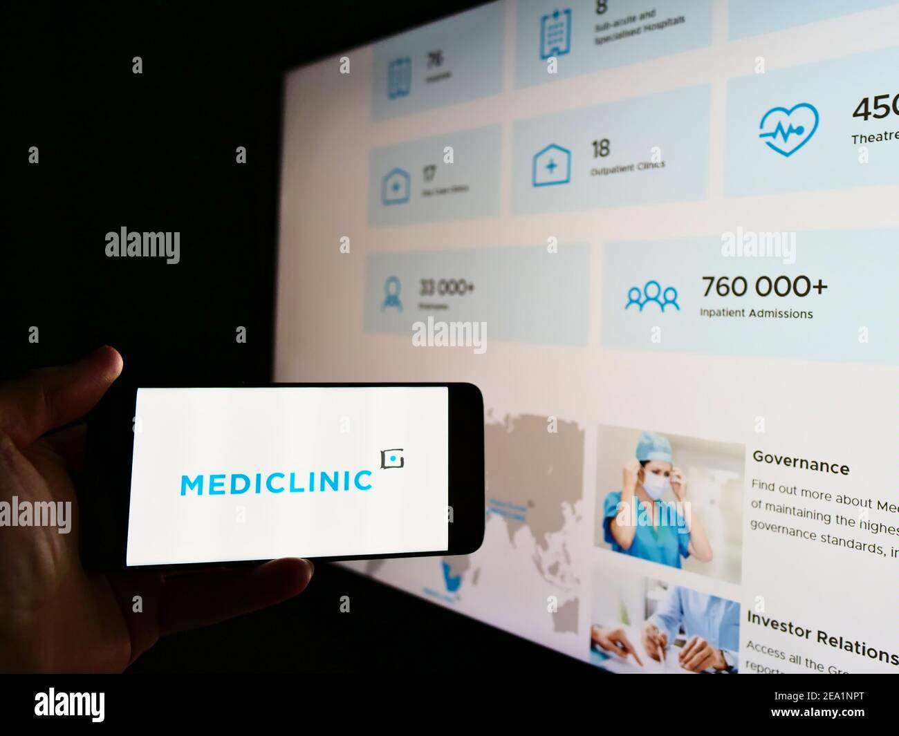 Person mit Mobiltelefon und Logo des Krankenhausbetreibers Mediclinic International plc auf dem Bildschirm vor der Webseite. Fokus auf Handy-Display. Stockfoto