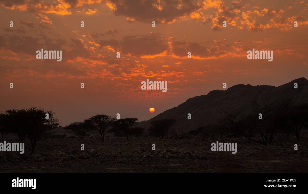 Wunderschöne Szene des Sonnenuntergangs hinter den kargen Bergen der Wüste in Ras Al Khaimah, Vereinigte Arabische Emirate. Feuerroter Himmel bei Sonnenuntergang. Stockfoto