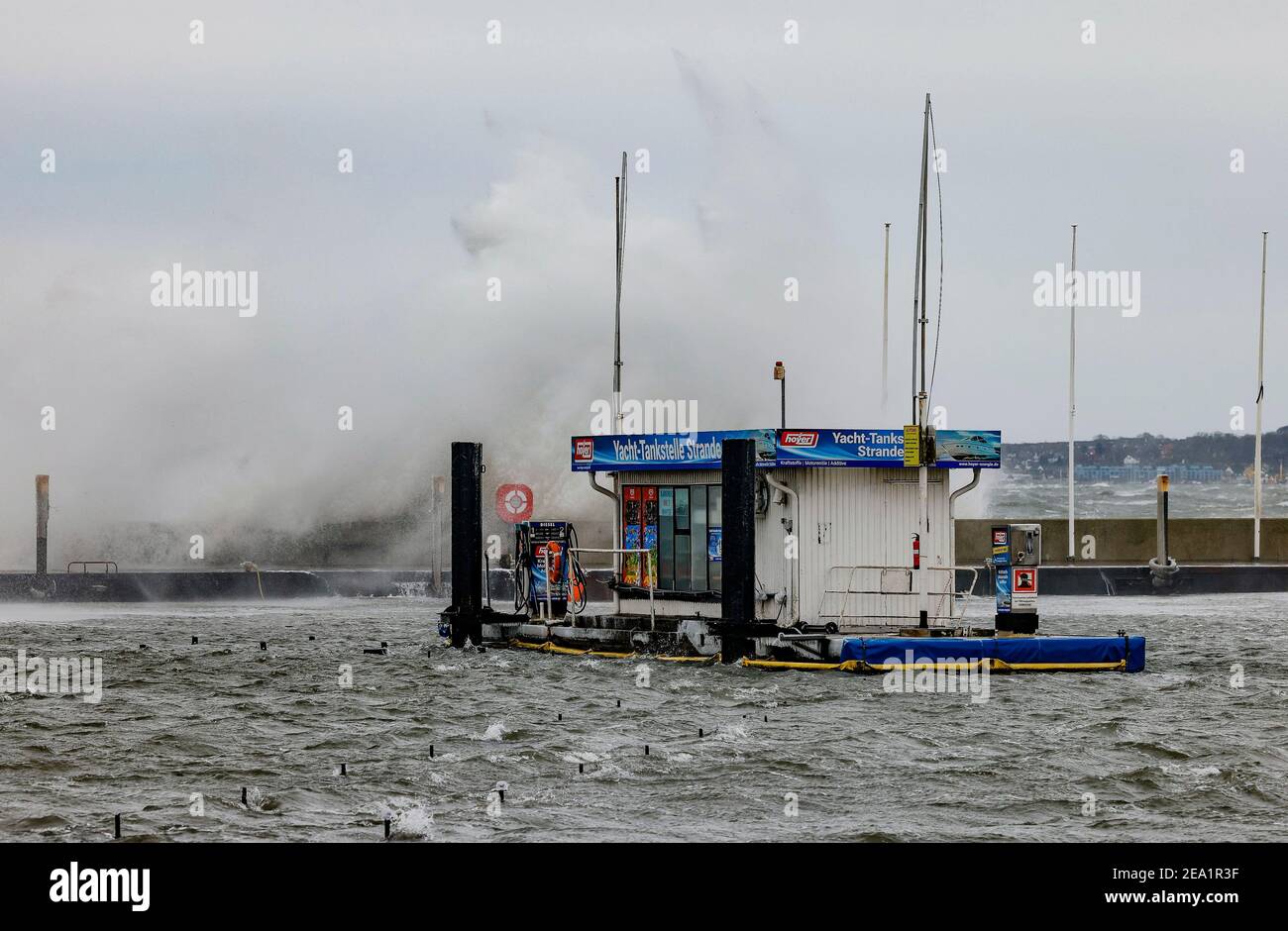 Strande, Deutschland. Februar 2021, 07th. Wellen krachen gegen die Hafenmauer hinter einer Bootsanlegestelle. Von Osten treffen bis zu 47 Knoten auf das Festland. Kredit: Frank Molter/dpa/Alamy Live Nachrichten Stockfoto