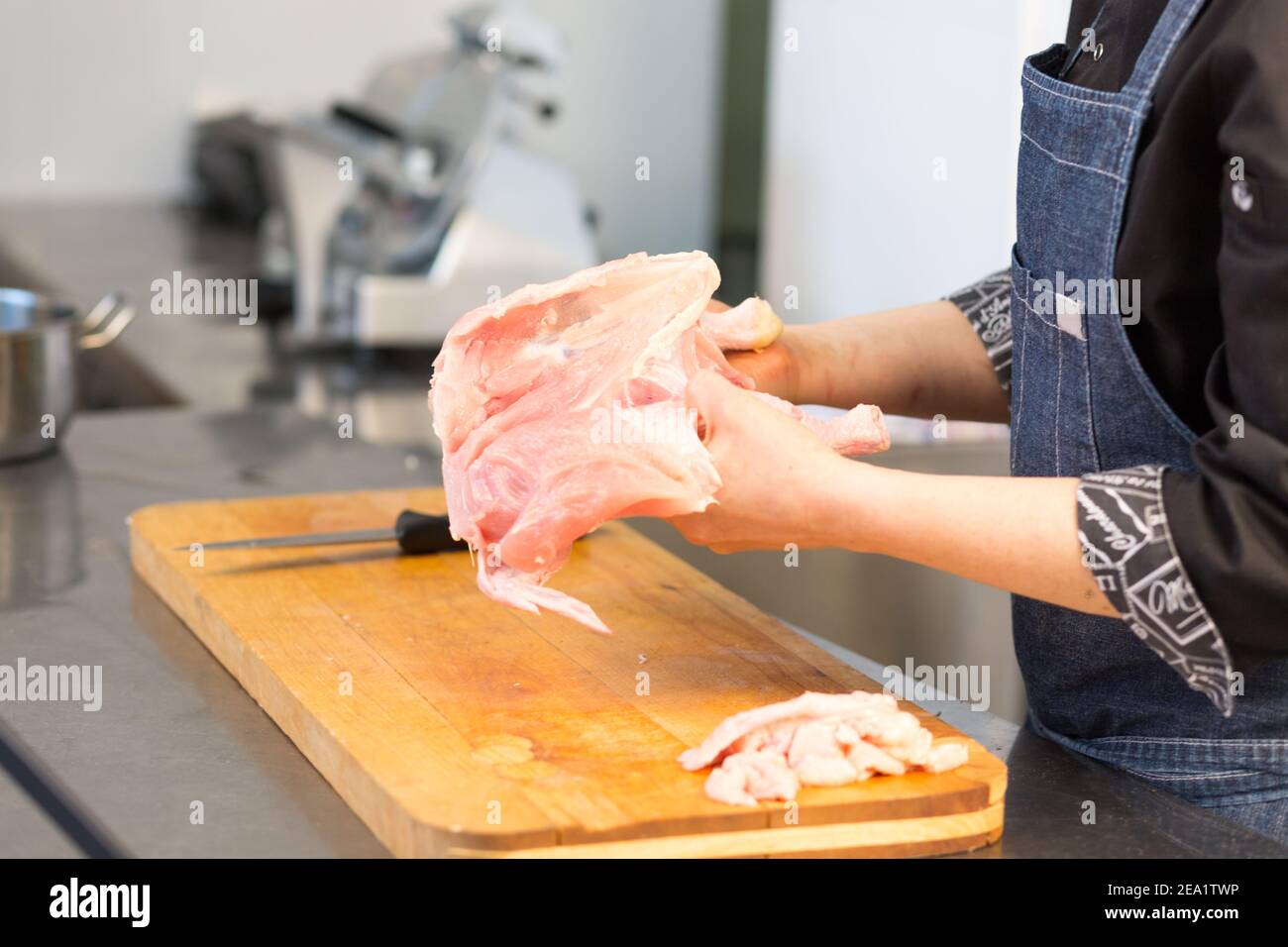 Eine Küchenchefin aus Kaukasian schneidet rohes Huhn. Master-Klasse. Cook's Hand mit einem Messer Nahaufnahme auf dem Hintergrund der Küche. Der Hintergrund ist unscharf Stockfoto