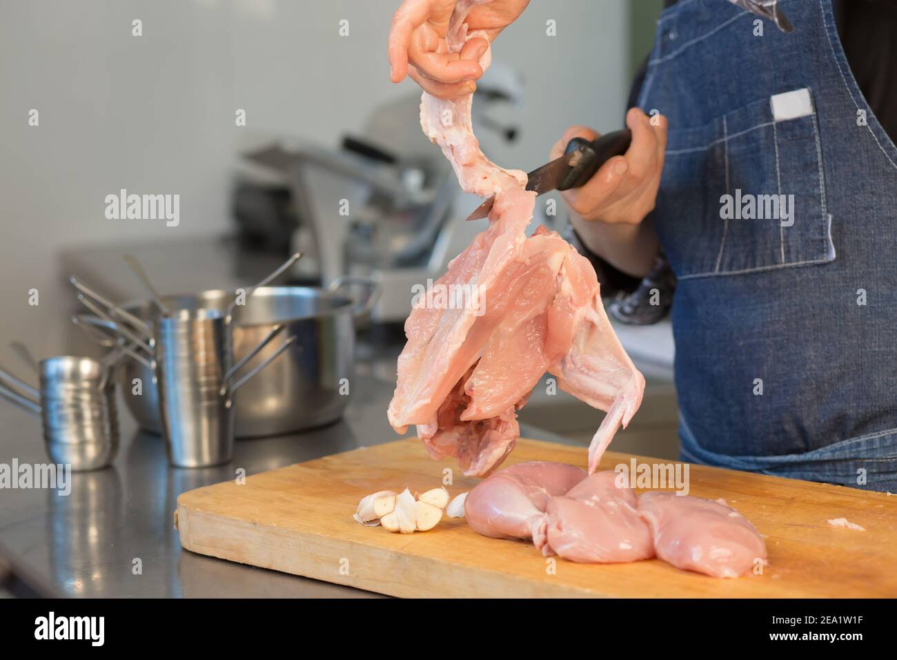 Nahaufnahme Rohes Huhn liegt portionsweise auf dem Brett in der Küche des Restaurants. Profi in schwarz Uniform Koch hält ein Messer. Master-Klasse Stockfoto