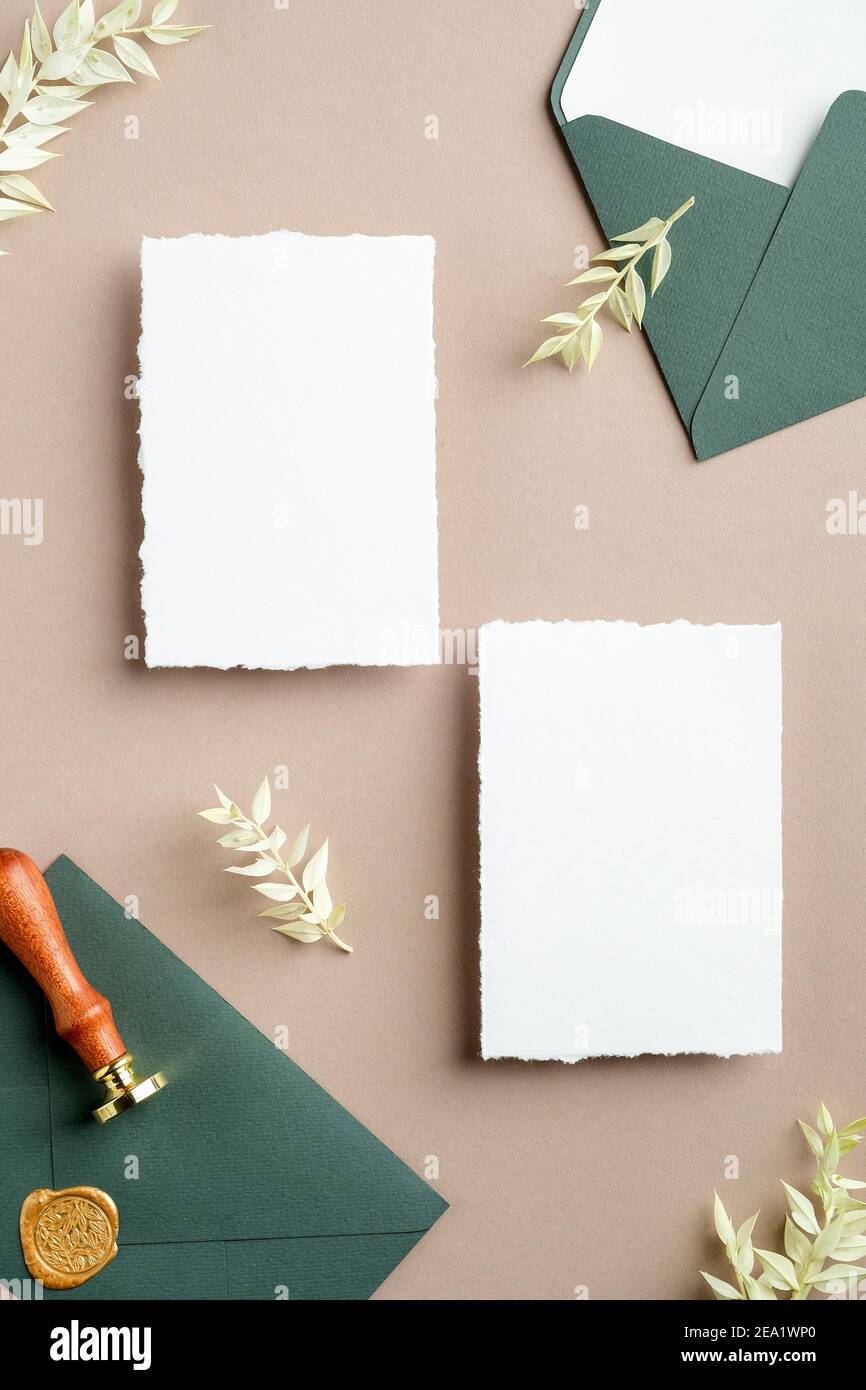 Flache Hochzeitseinladungskarten, grüner Umschlag mit Siegelwachs-Stempel, getrocknete Blumen auf pastellbeigem Hintergrund. Hochzeits-Schreibwaren Set Draufsicht. Stockfoto