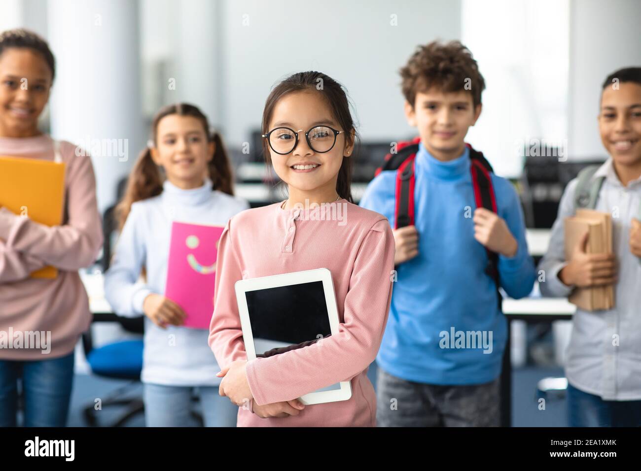 Lächelnd asiatische Mädchen halten Tablette stehen mit Klassenkameraden Stockfoto